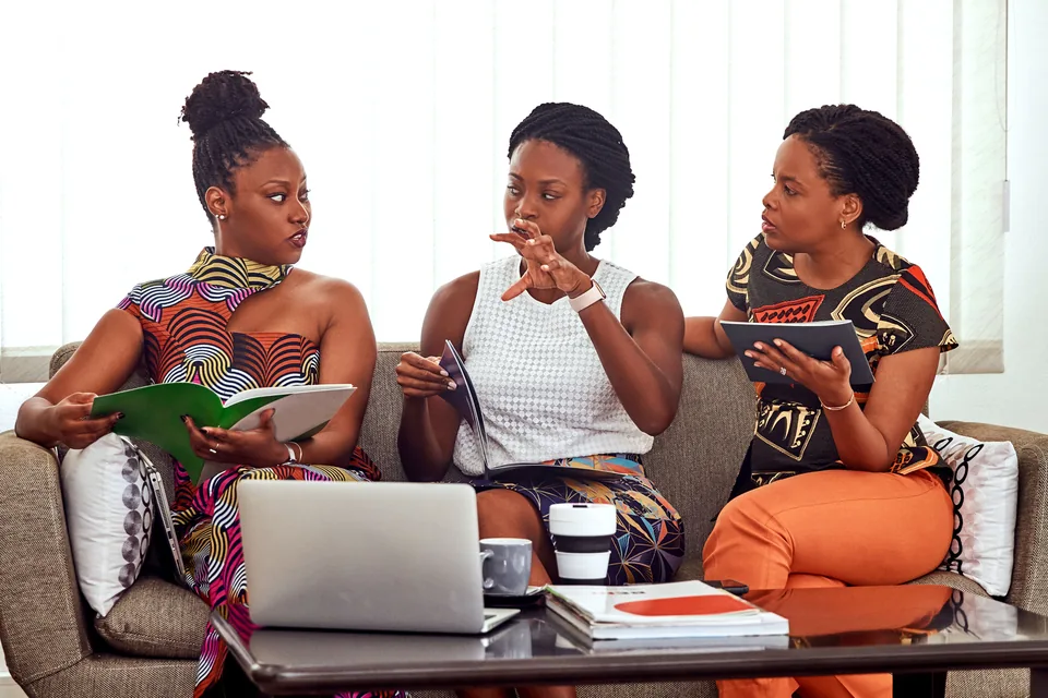 Three African women discussing work with notebooks and a laptop